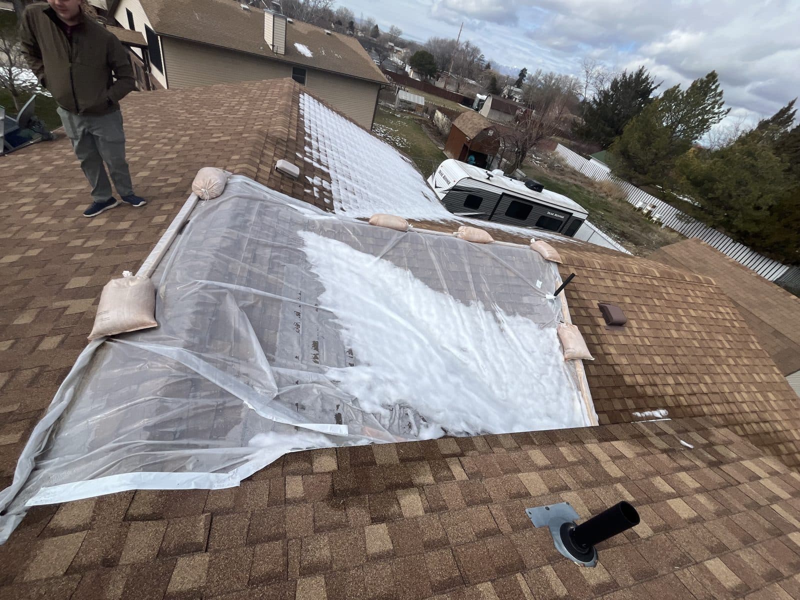Clear plastic emergency cover held down with sandbags over a section of roof, with snow on the shingles.