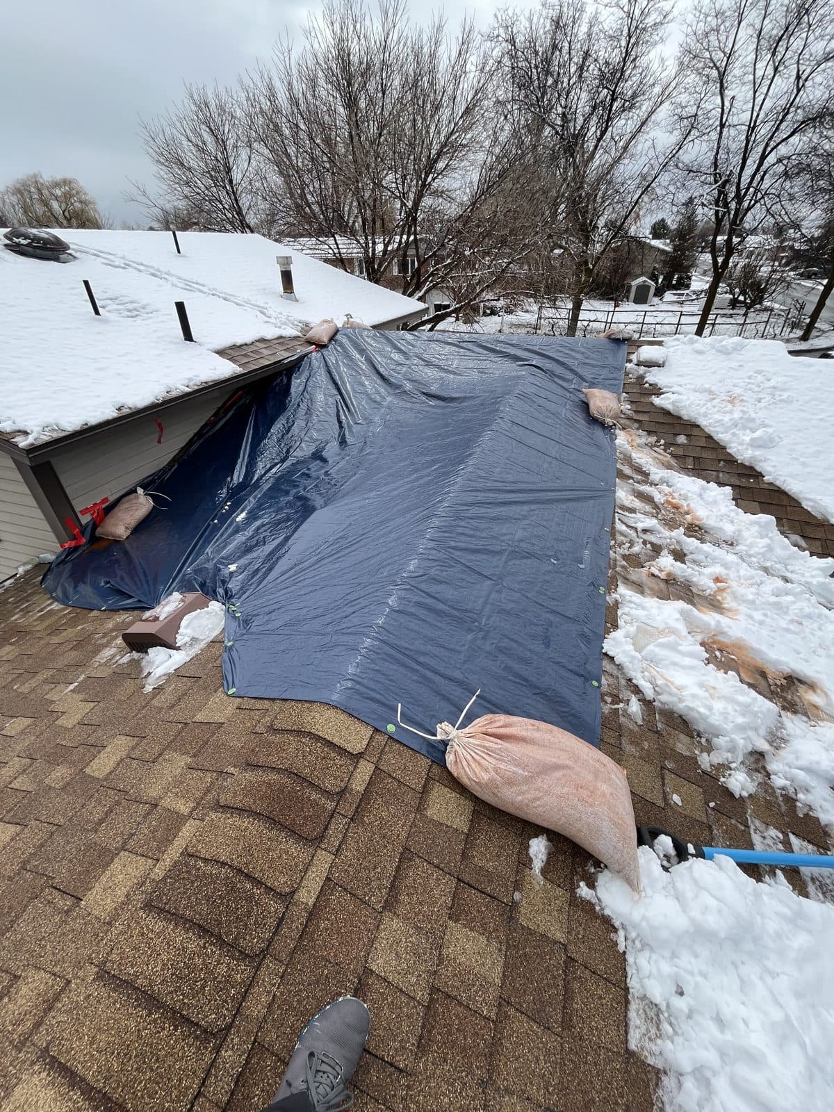 Blue emergency tarp weighted with sandbags on a snow-covered roof.