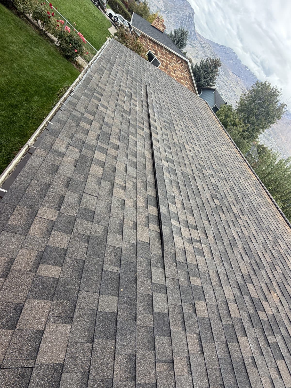 Finished architectural asphalt shingle roof in a brown and tan blend, with the Wasatch mountains behind the ridge.