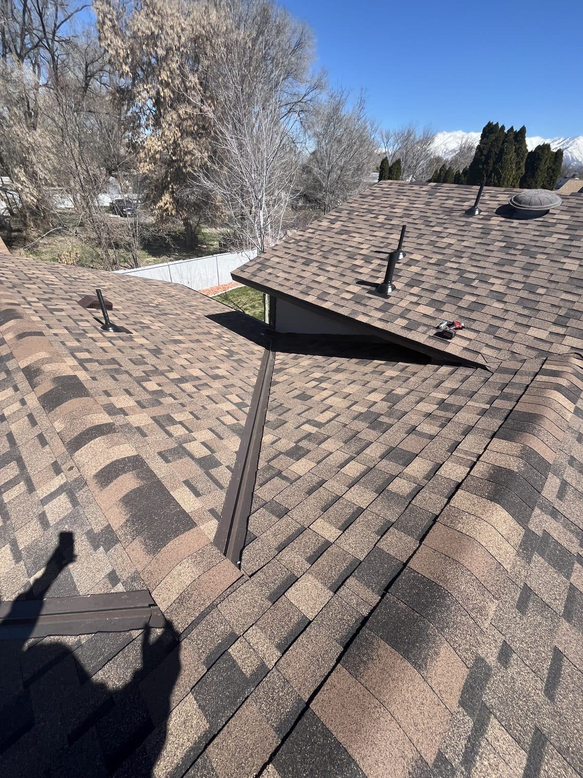 Finished architectural shingle roof with a metal valley and snowy mountains behind the ridge.