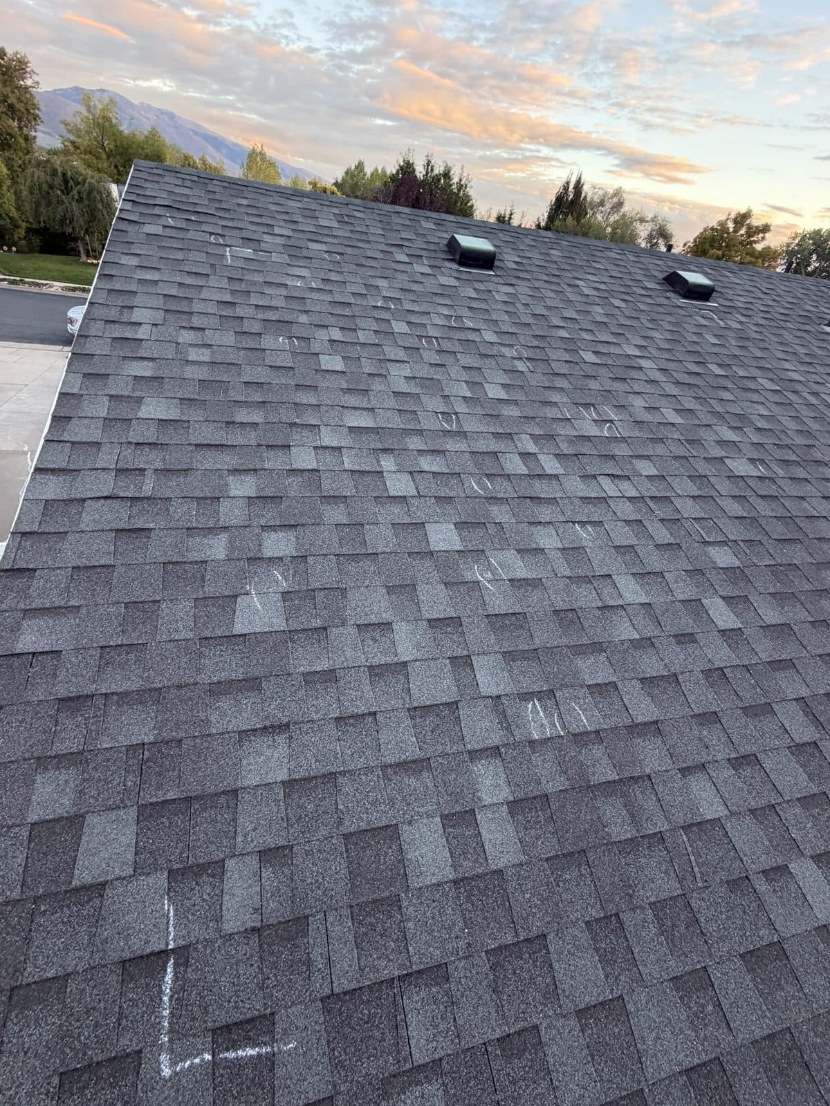 Hail inspection on a gray asphalt shingle roof, with chalk circles marking impact hits.