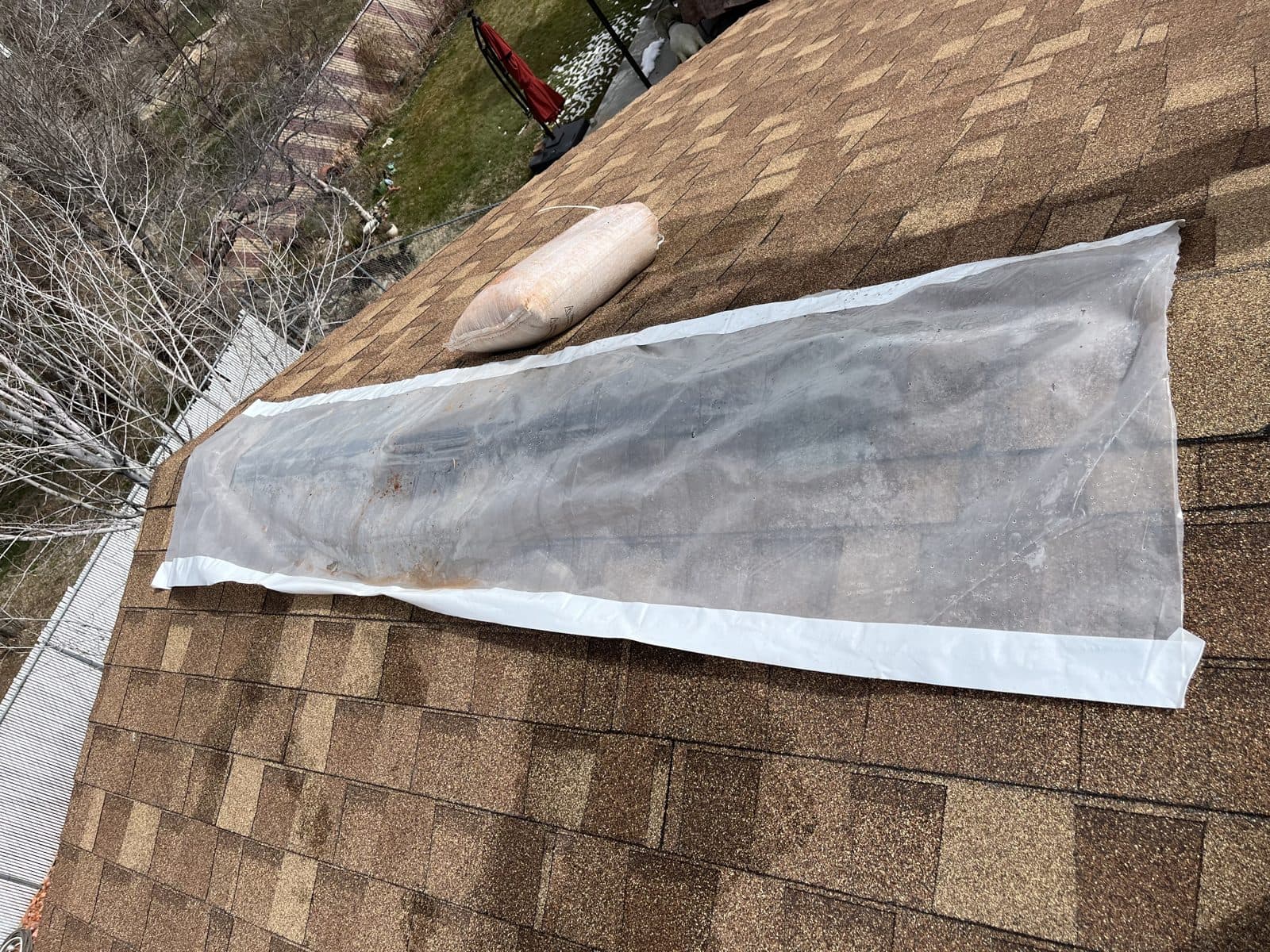 Temporary underlayment patch taped over a cleared area of an asphalt shingle roof.