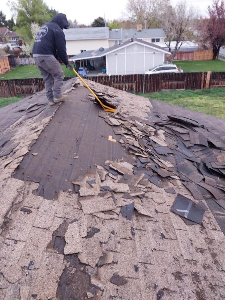 Worker stripping old asphalt shingles off a roof during tear-off.