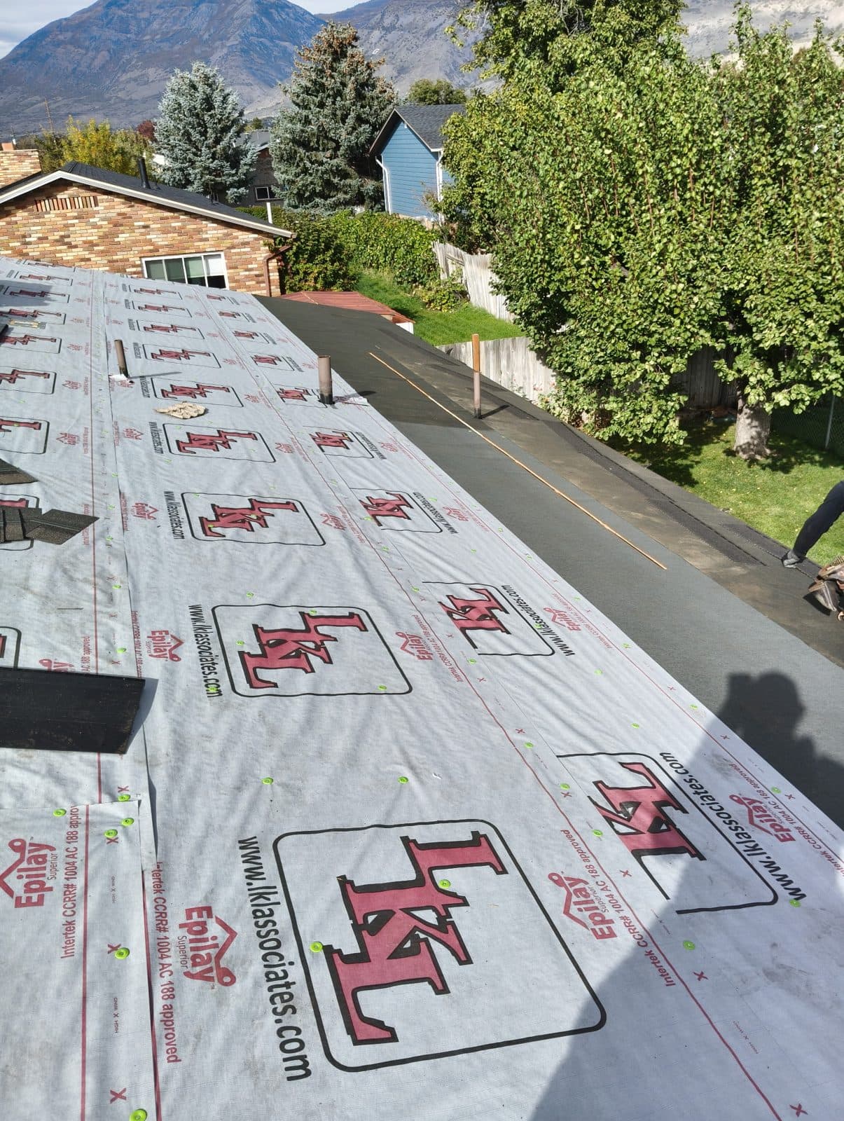 Synthetic underlayment covering a roof during a replacement, with mountains behind the house.