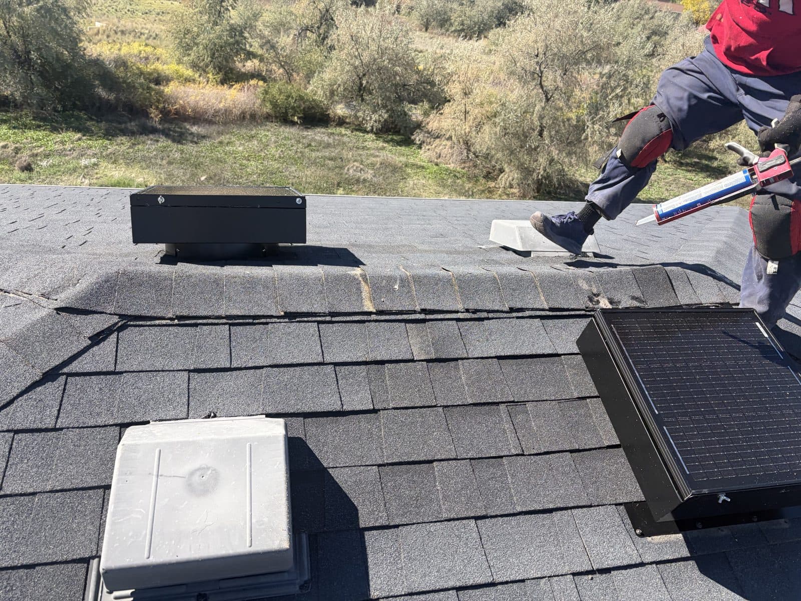 Roof repair sealing around attic vents and a solar attic fan, with a cracked ridge cap still on the roof.